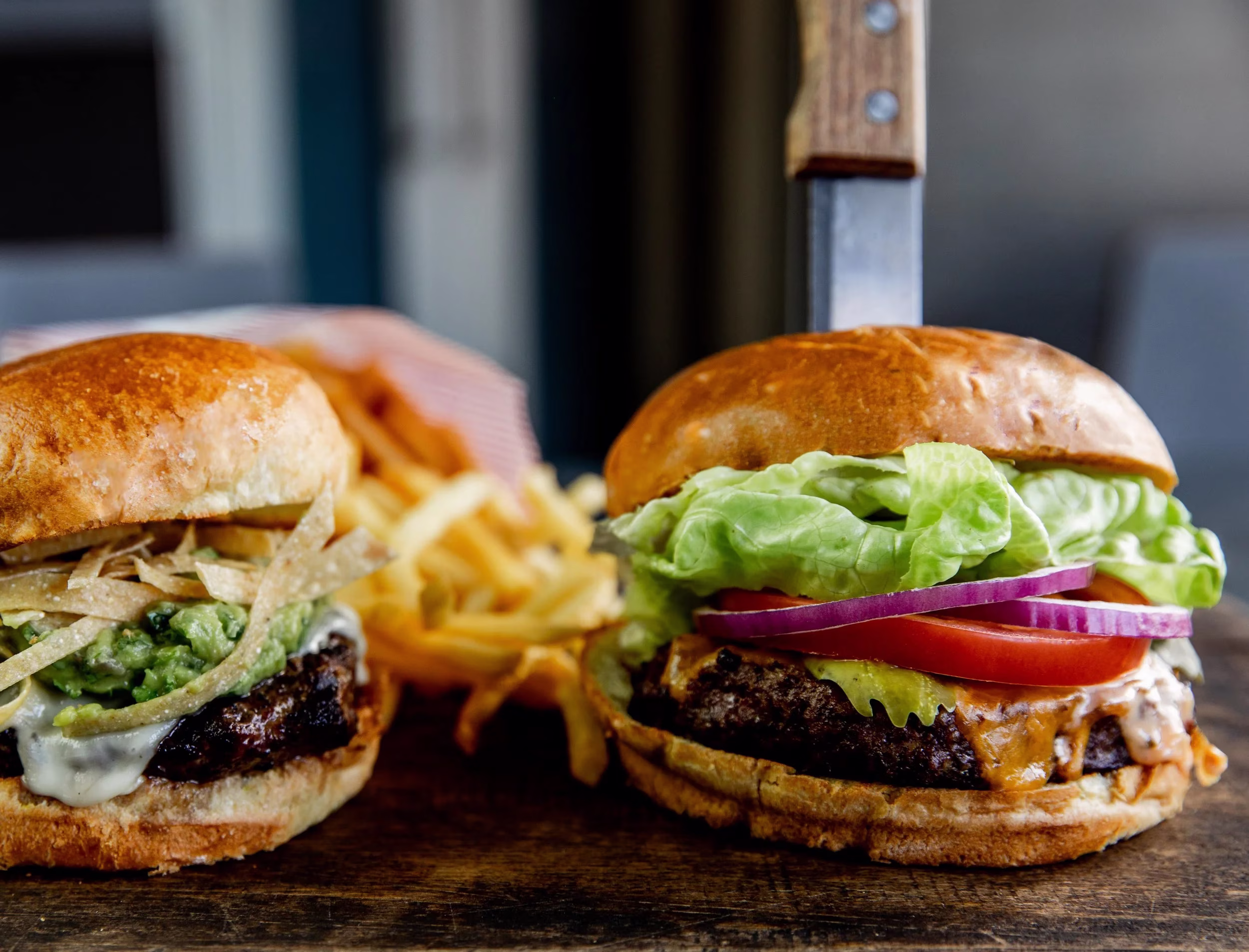 Two burgers and fries on a wooden board, one with a knife.