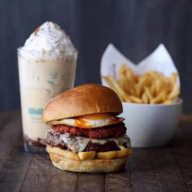 Large burger with fried egg, cheese, and fries, plus a milkshake.