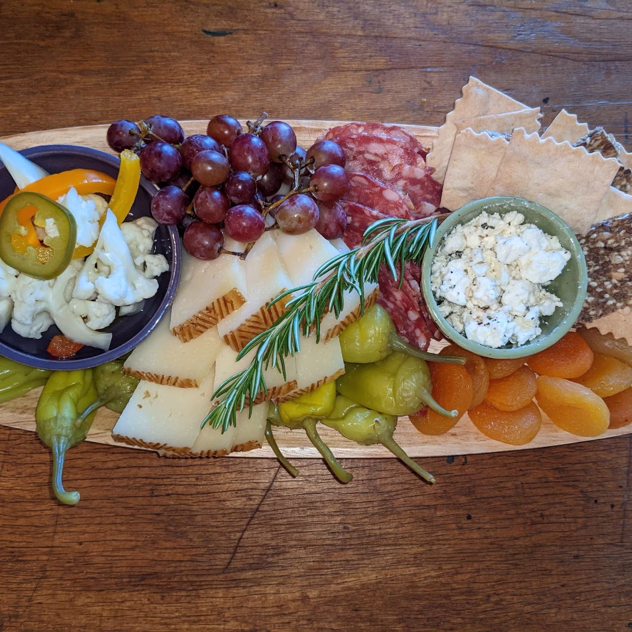 Charcuterie board with cheese, grapes, salami, crackers, and pickled vegetables.