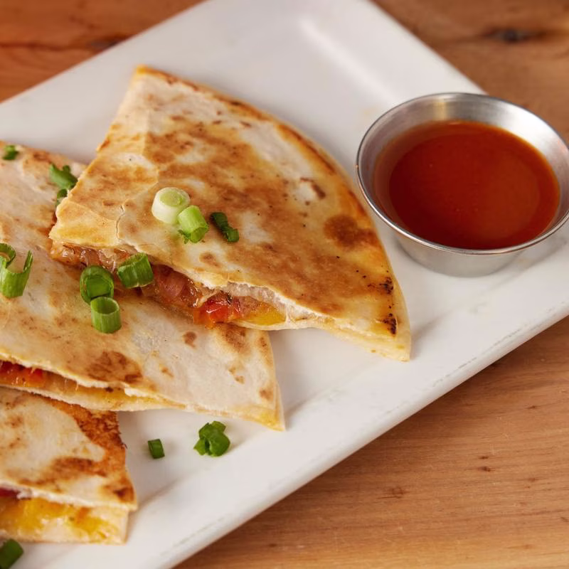 Quesadilla slices topped with green onions and a side of red sauce.
