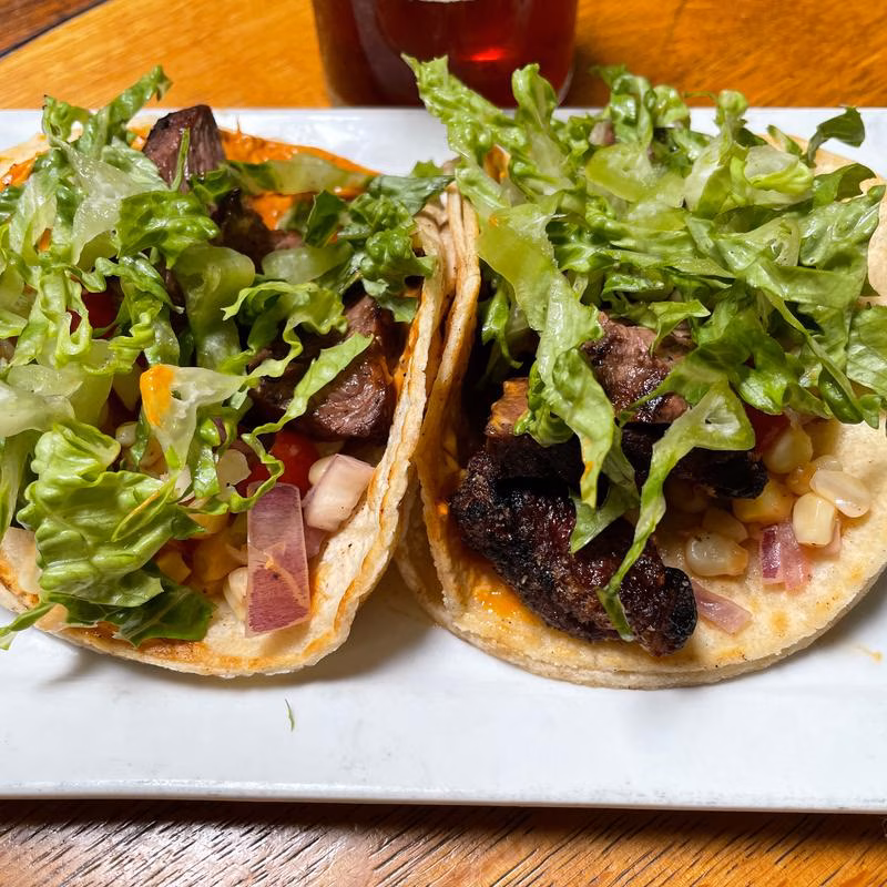 Two street tacos with steak, lettuce, corn, and red onion.