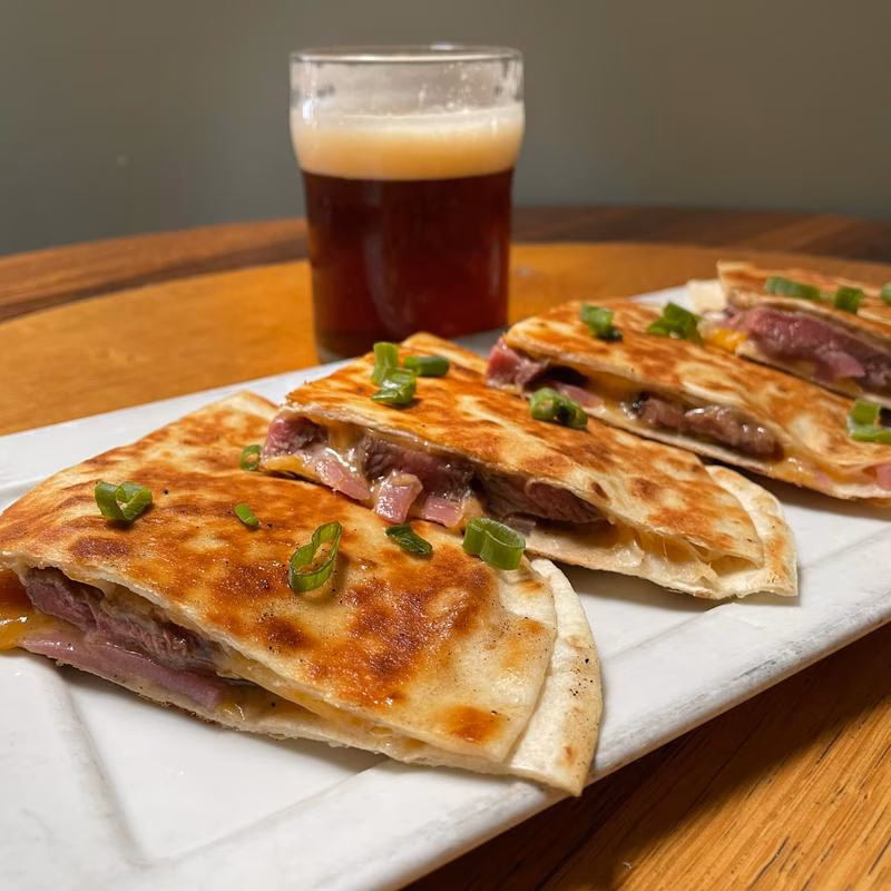 Steak and cheese quesadillas with chives and a glass of dark beer.