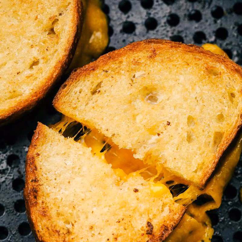 Toasted golden grilled cheese sandwich cut, showing stretching melted cheese.