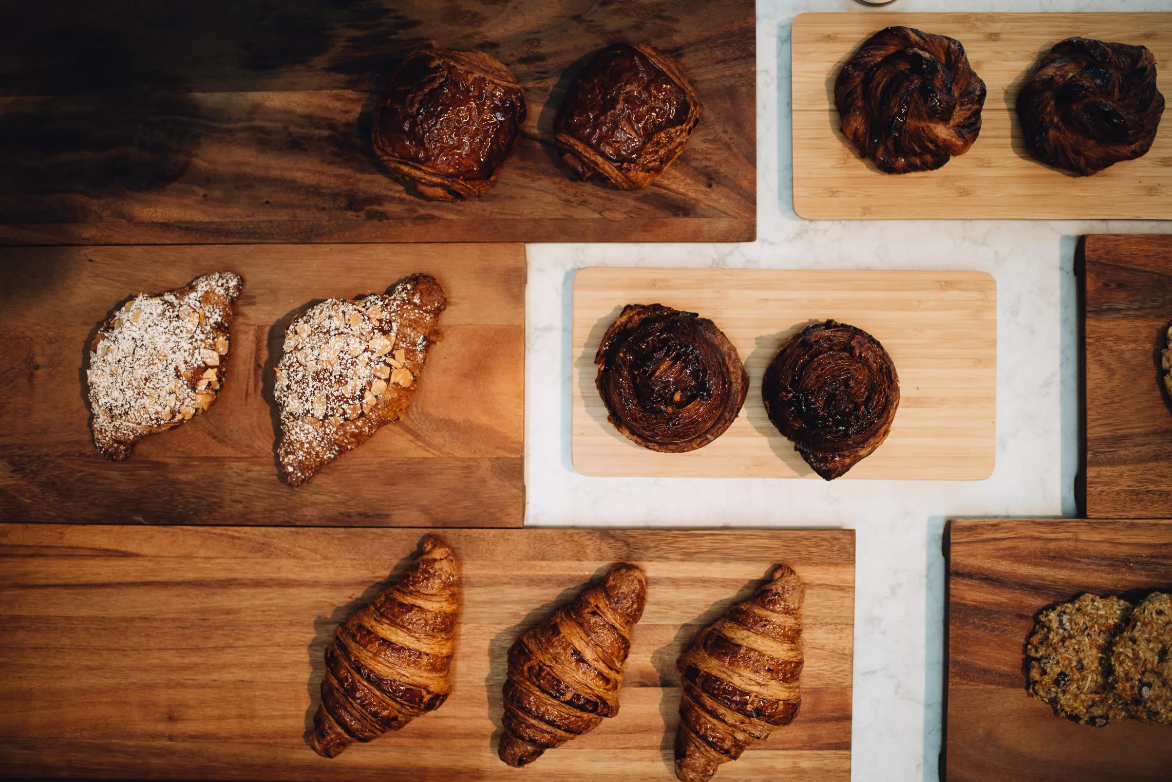 Assorted pastries and cookies displayed on wooden boards and white counter.
