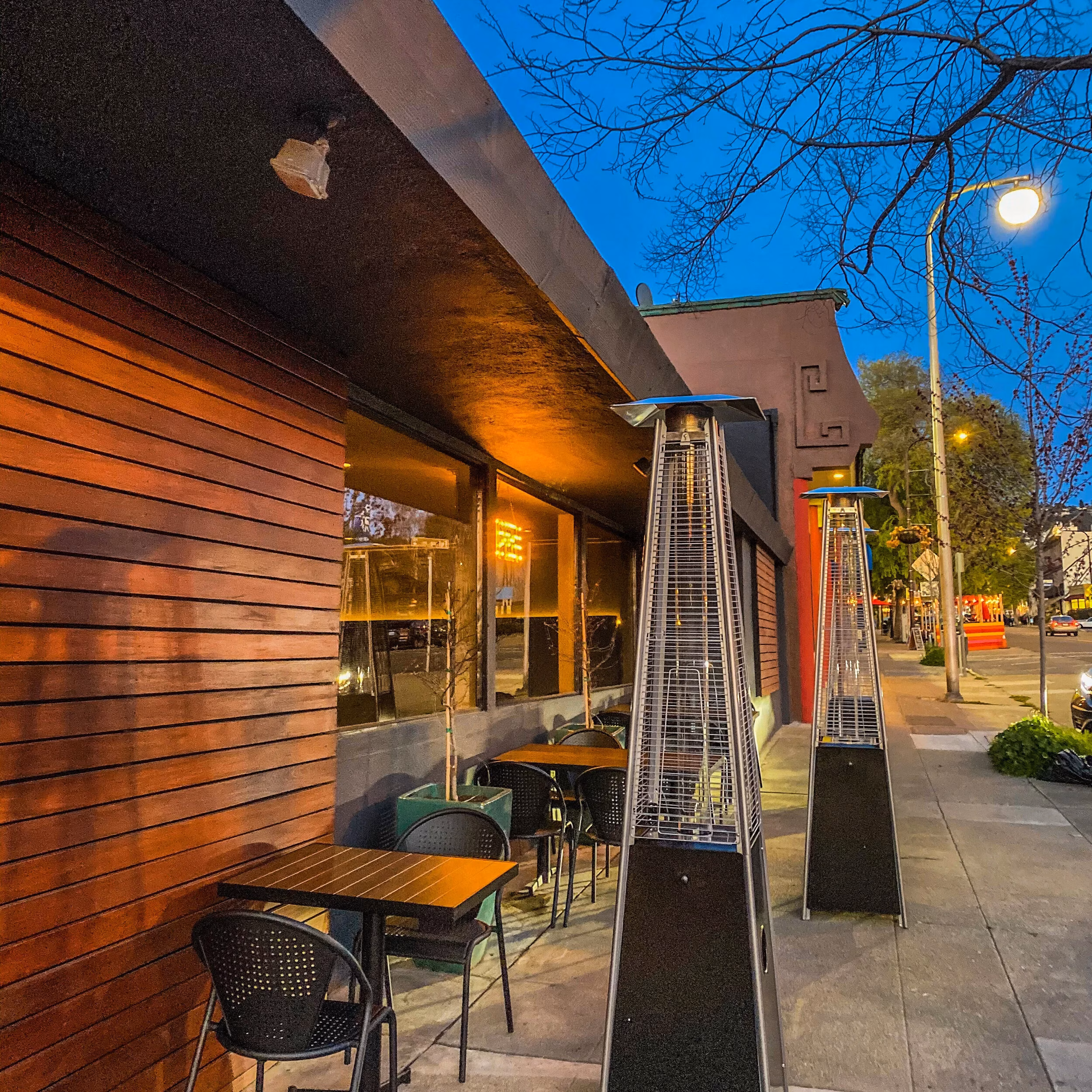 Outdoor dining patio with heaters, tables, and chairs at twilight.
