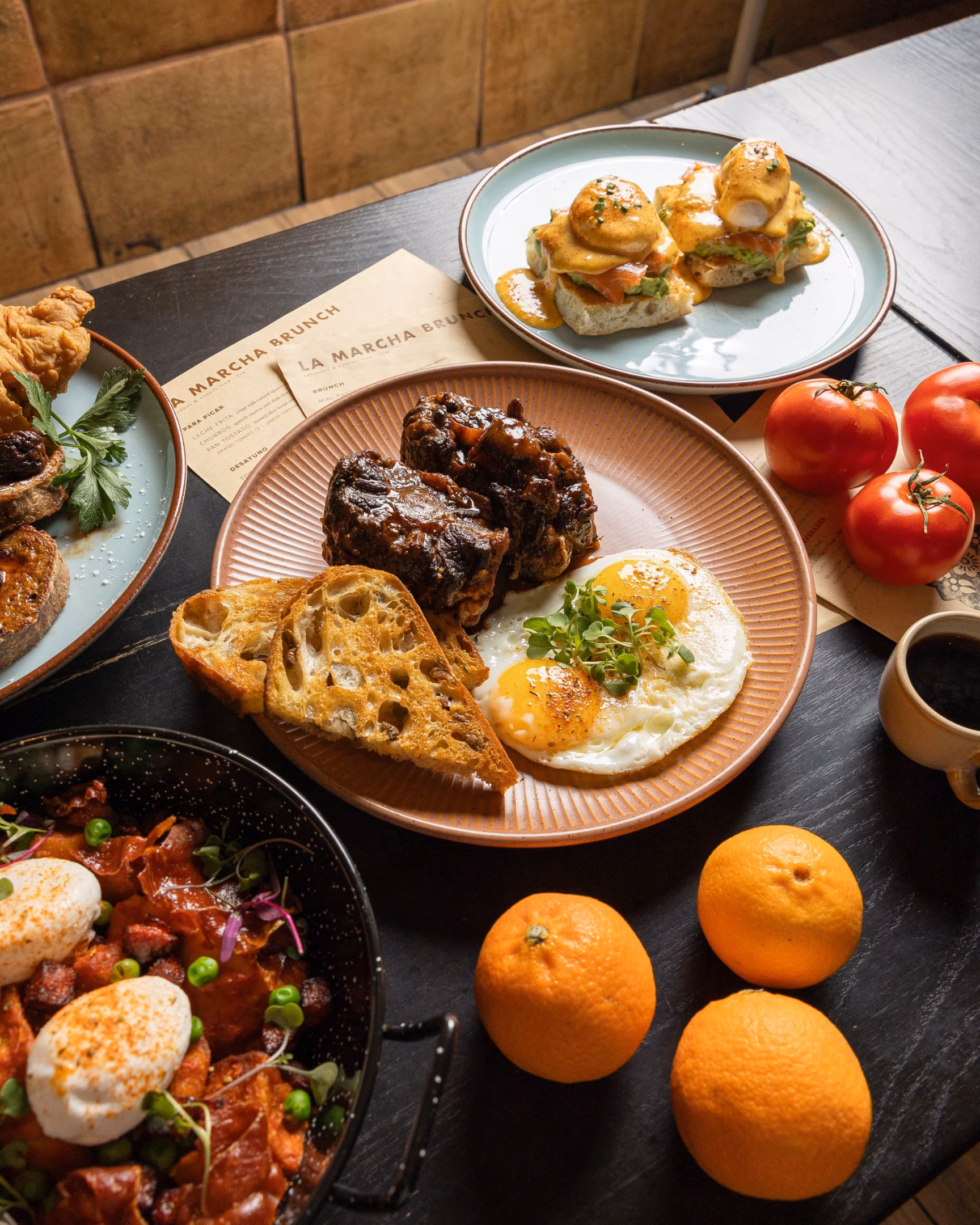 Overhead shot of various brunch dishes, oranges, and tomatoes on a table.