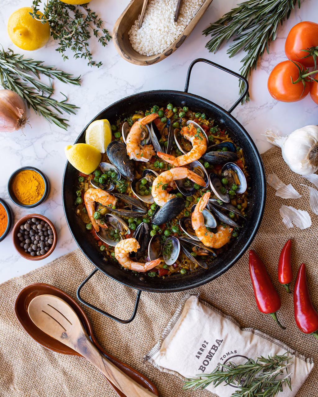 Seafood paella in a pan with lemons, herbs, spices, and peppers.