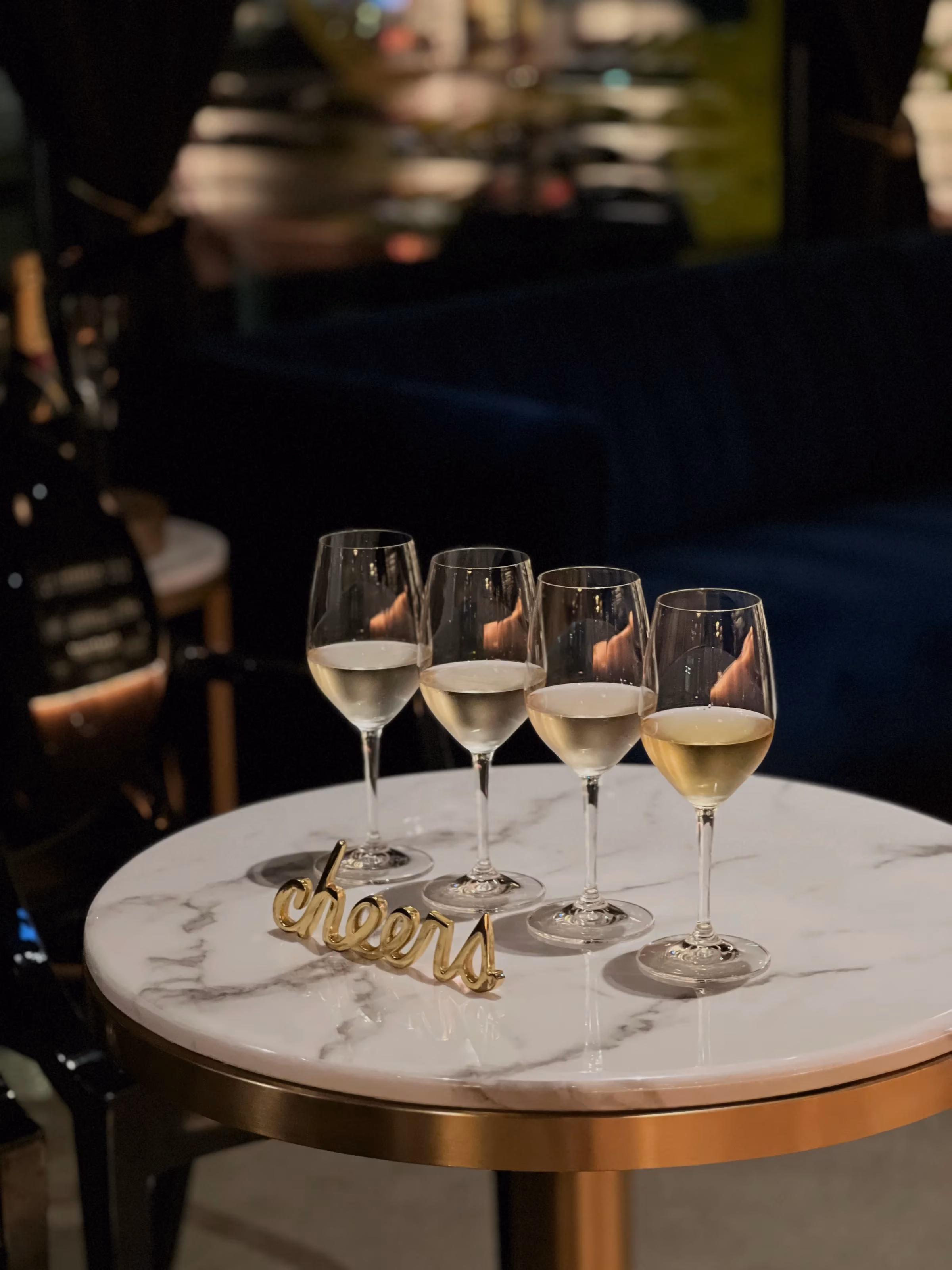 Four white wine glasses on a marble table with a "cheers" sign.