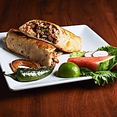 Two burritos, watermelon, lime, and green chili on a white plate.