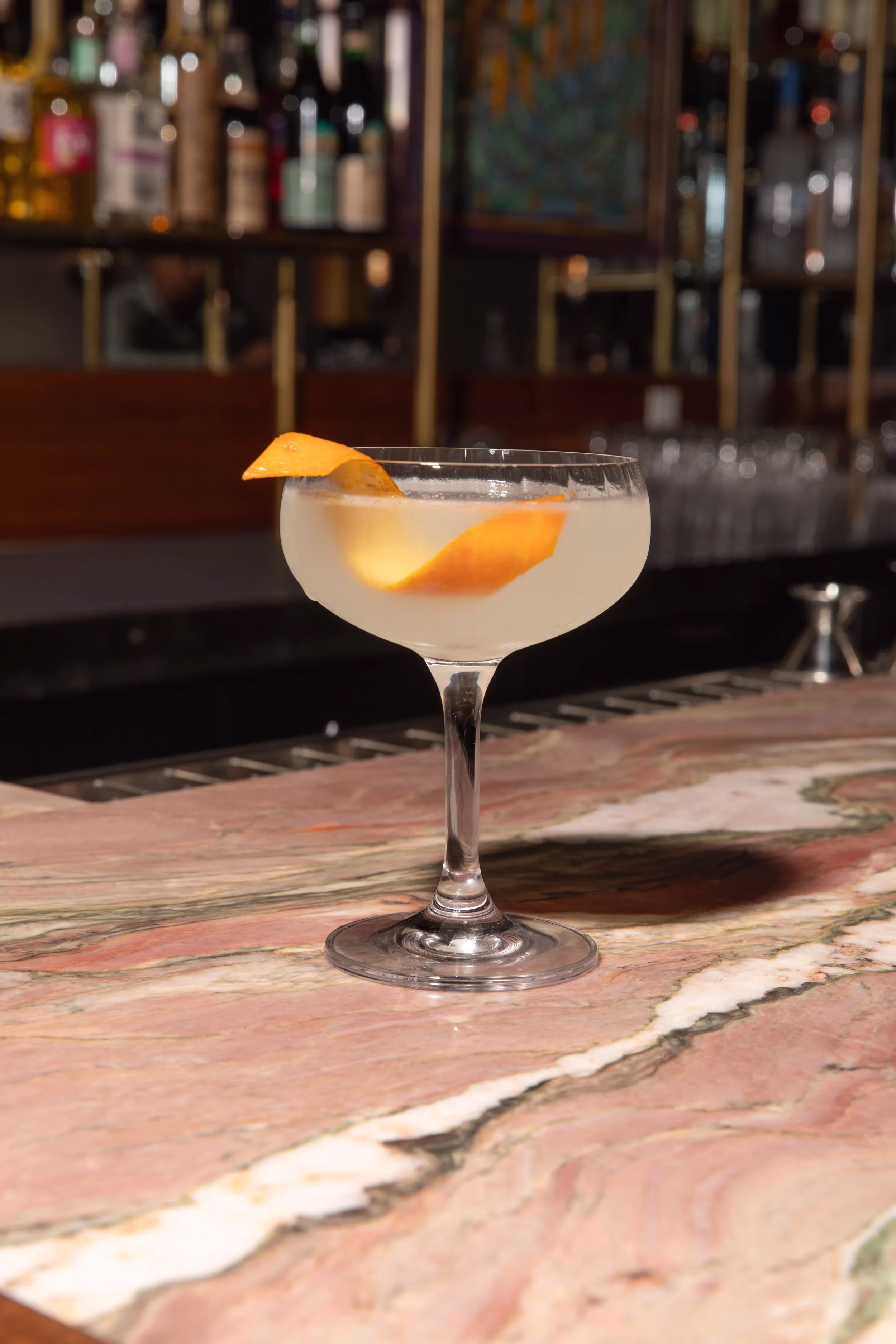 A white cocktail in a coupe glass with an orange peel garnish.
