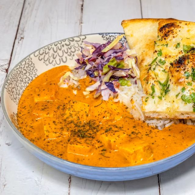 Bowl of orange curry, rice, chopped cabbage, and herbed flatbread.