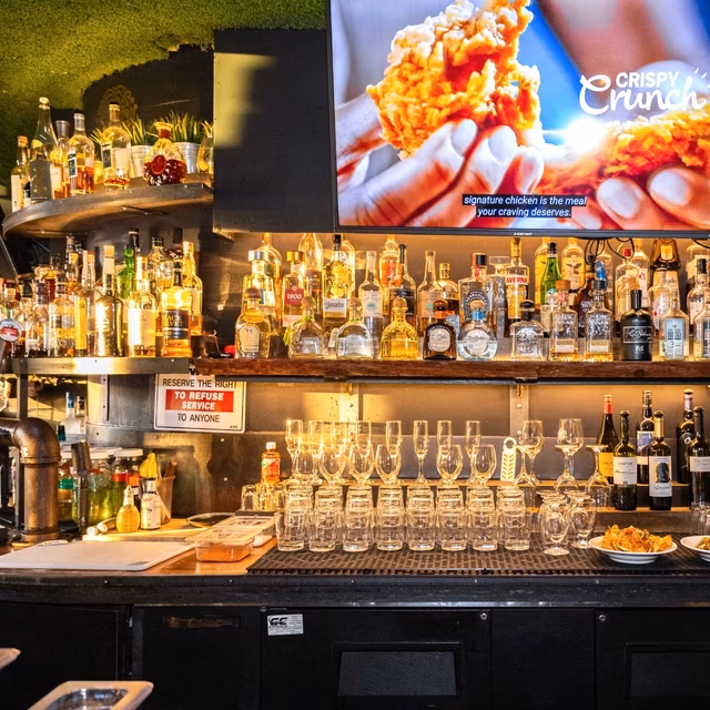 Bar interior with liquor bottles, stacked glasses, and a TV screen.