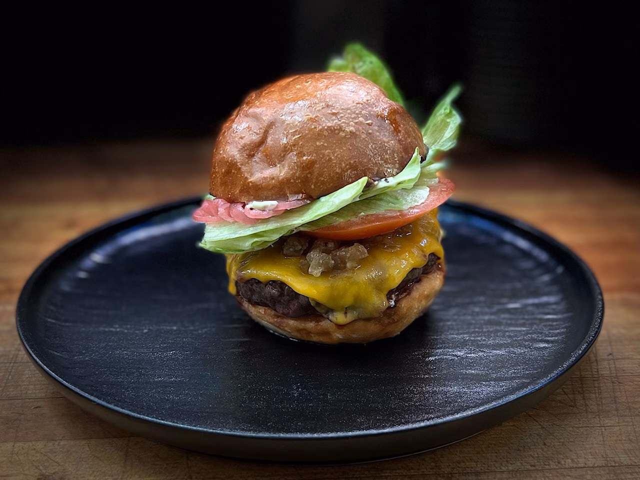 Hamburger with cheese, onions, tomato, and lettuce on a black plate.