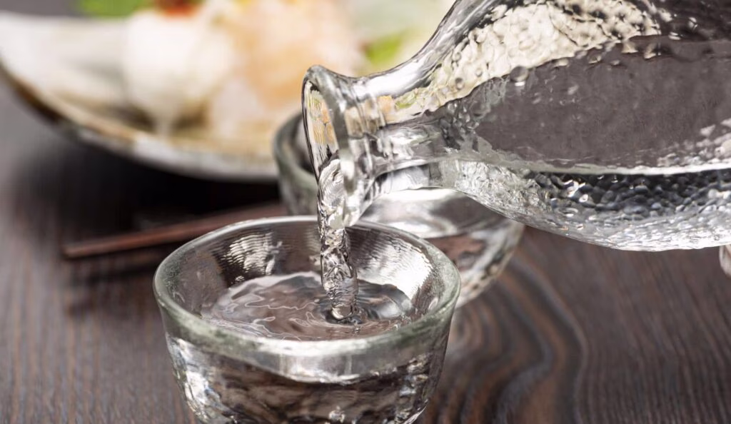 Clear liquid being poured from glass carafe into a small cup.