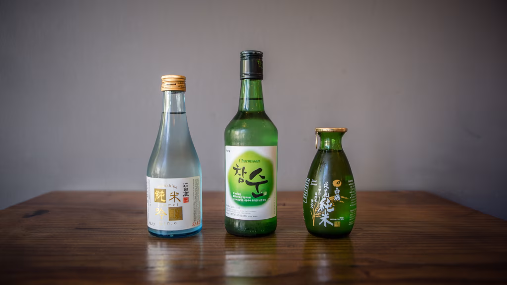 Three bottles of sake and soju on a wooden table.