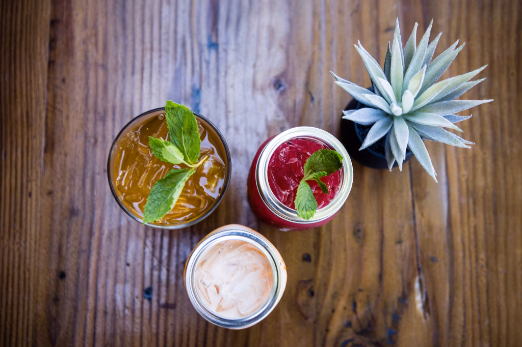 Three iced drinks and a potted succulent on a wooden table.