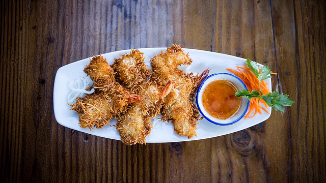 Crispy coconut shrimp with dipping sauce and garnish on a white plate.