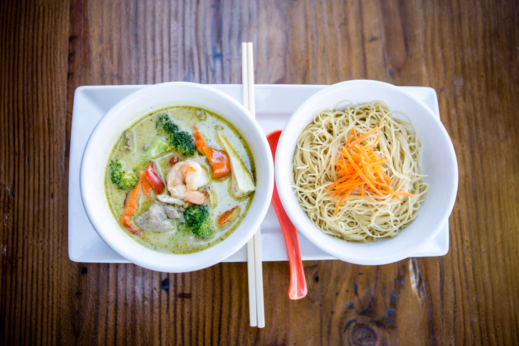 Green curry with shrimp and noodles with carrots on wooden table.