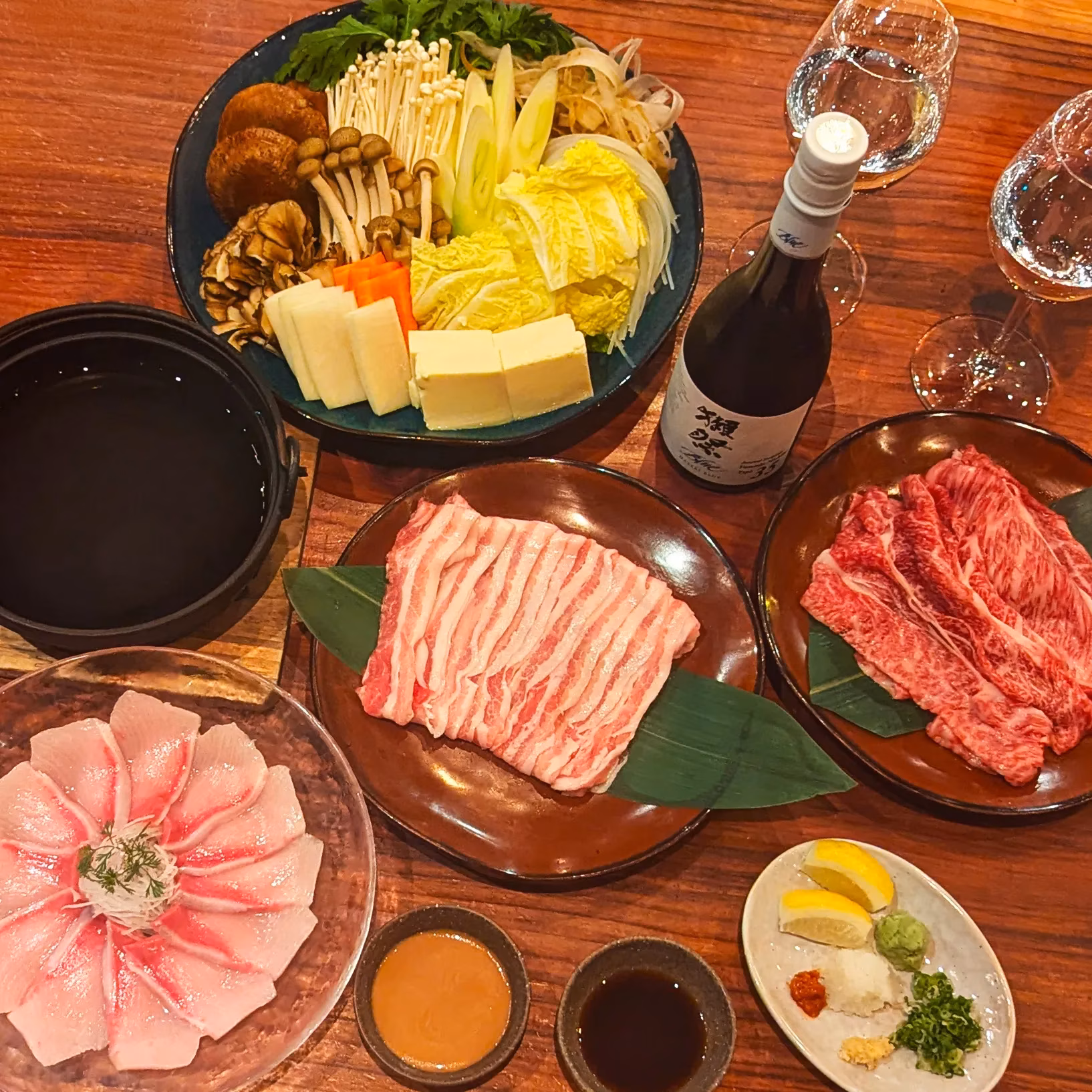 Japanese hot pot meal with raw meats, fish, vegetables, and sake.