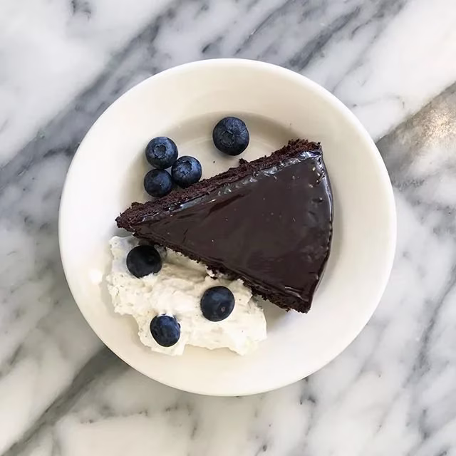 A slice of chocolate cake with blueberries and whipped cream on a white plate.