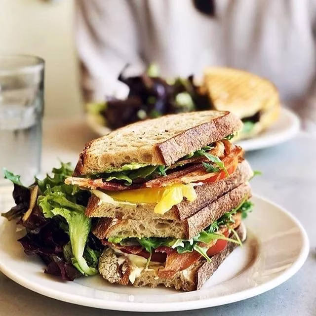 Multi-layered sandwich with bacon, greens, tomato, yellow layer, and salad.