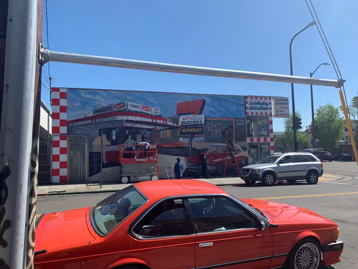 Mural of 1950s diner and classic cars being painted on building.