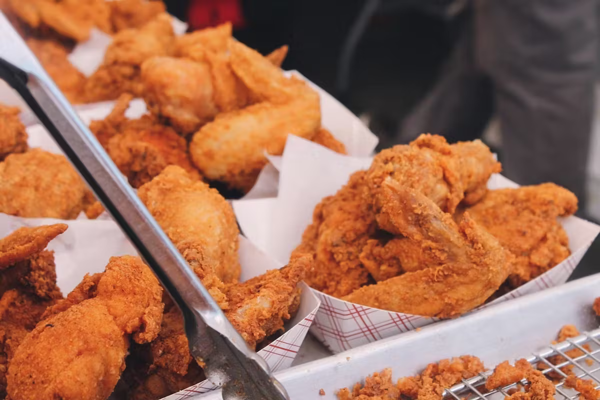 Numerous golden fried chicken pieces in paper trays with tongs.