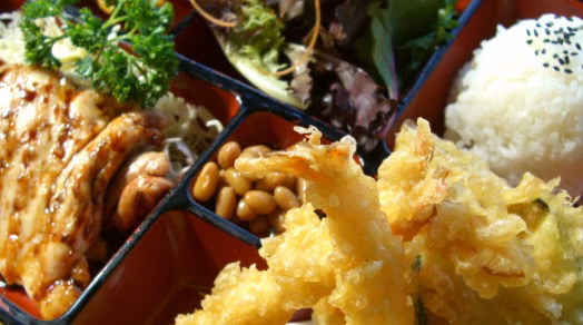Japanese bento box with chicken, tempura, rice, salad, and beans.