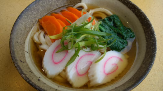 Udon noodle soup with narutomaki, carrots, spinach, and green onions.