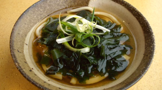 Bowl of udon noodles with wakame seaweed and green onions.