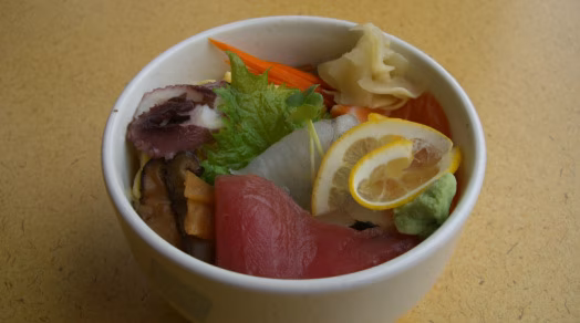 Bowl of sashimi and vegetables, with lemon, ginger, and wasabi.