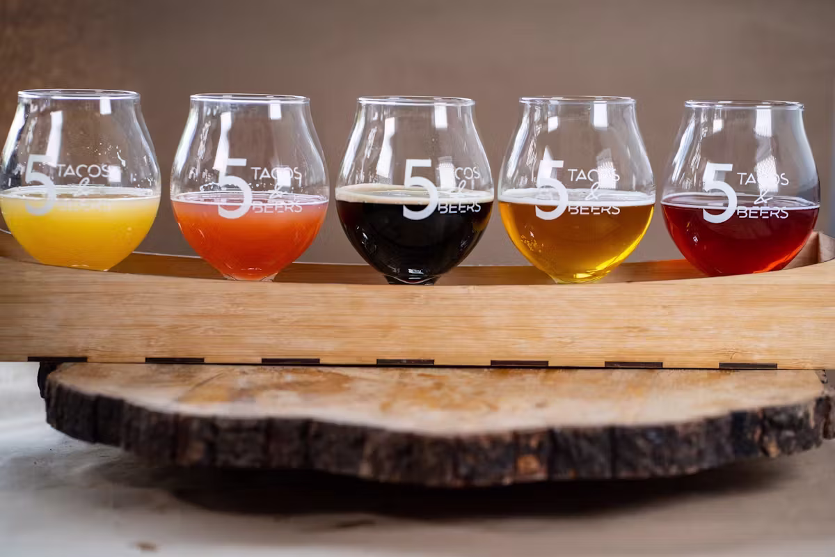 Five glasses of different colored beers on a wooden paddle.