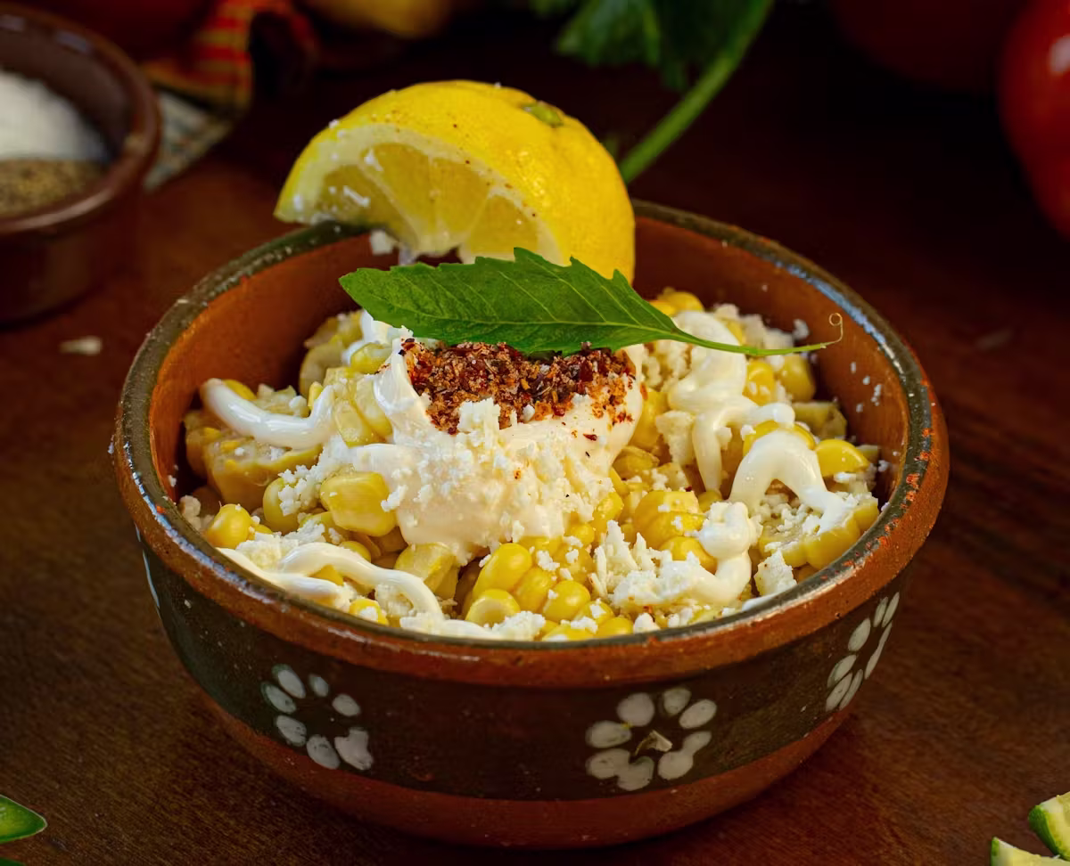 Bowl of corn kernels with creamy sauce, crumbled cheese, spice, and lime.
