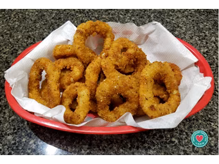 Golden-brown fried onion rings in a red basket lined with paper.