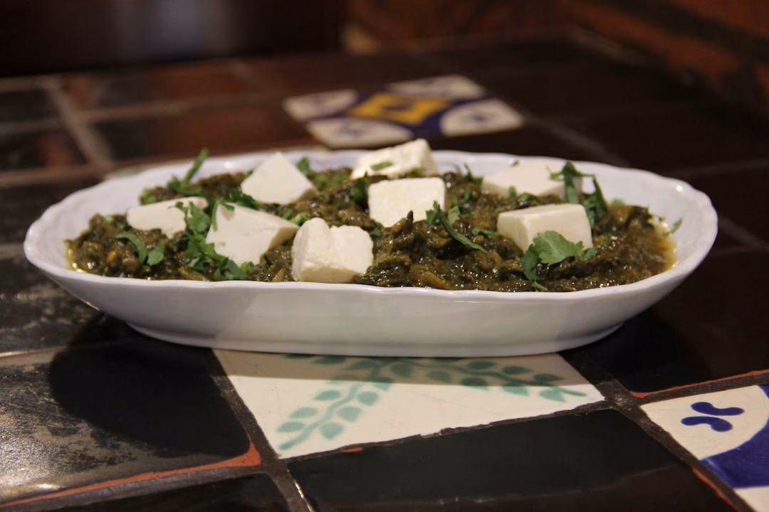 White oval dish filled with green stew, white cheese, and herbs.