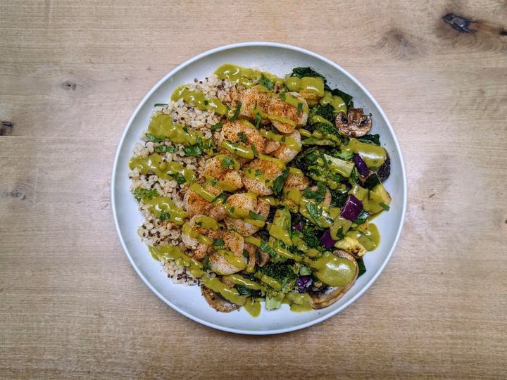 Shrimp, quinoa, vegetables, and green sauce in a white bowl.