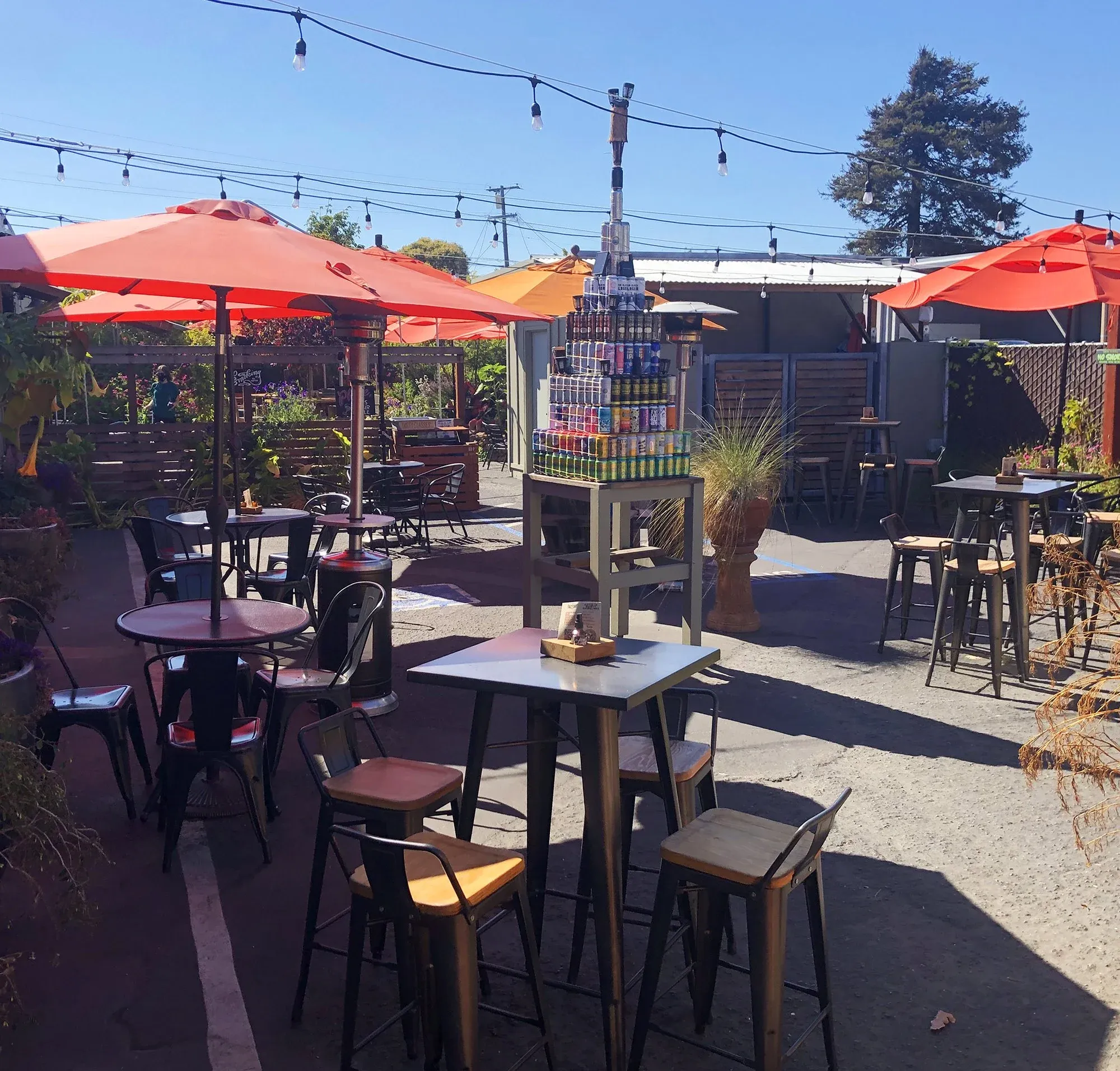 Outdoor patio with orange umbrellas, tables, and stacked beverage cans.