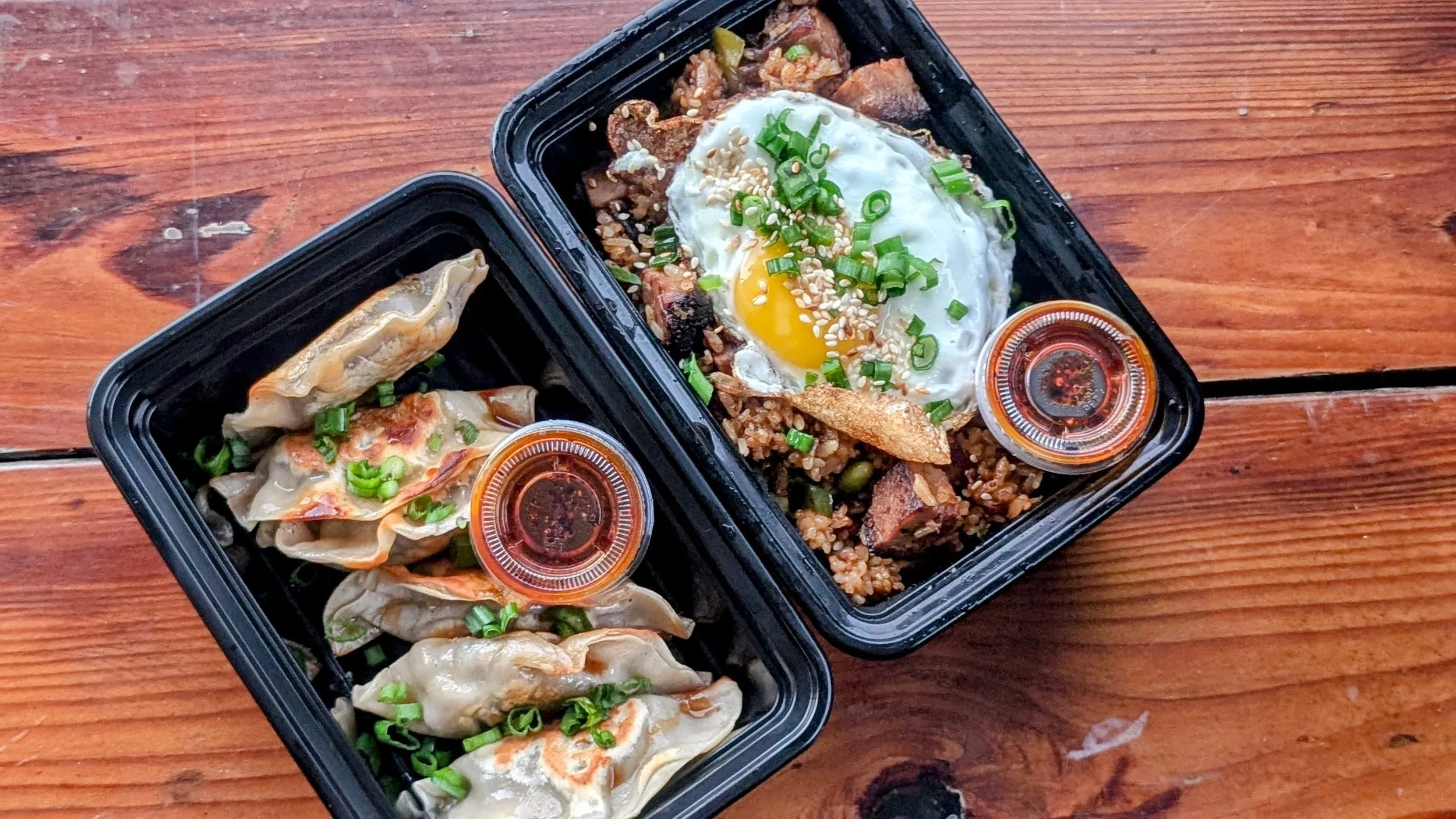 Takeout containers with pan-fried dumplings and fried rice with egg.