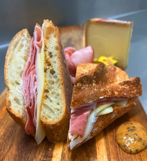 Sliced baguette sandwich with ham, cheese, and mustard on a board.