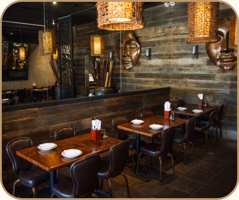 Restaurant interior with wooden walls, dining tables, decorative masks, and woven lamps.