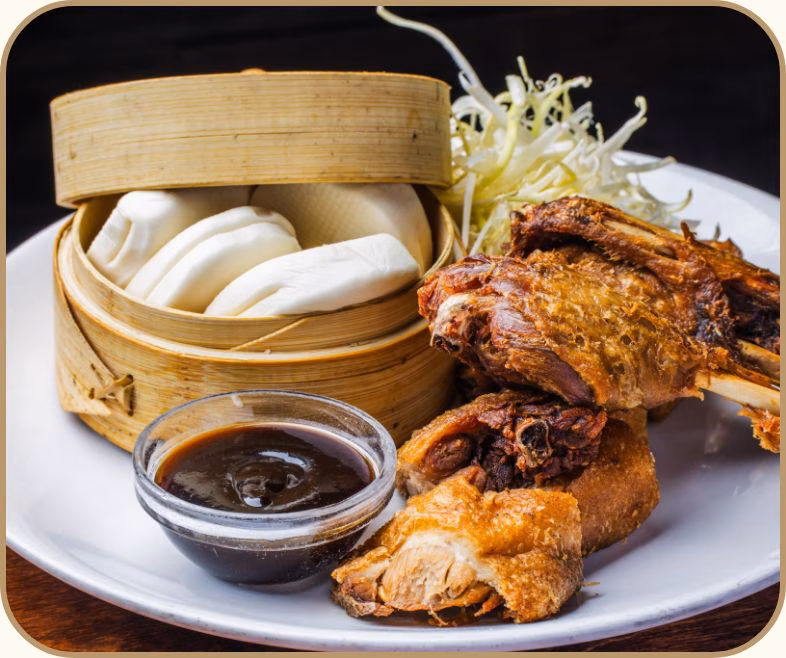 Crispy fried meat, steamed white buns, dark dipping sauce, shredded greens.