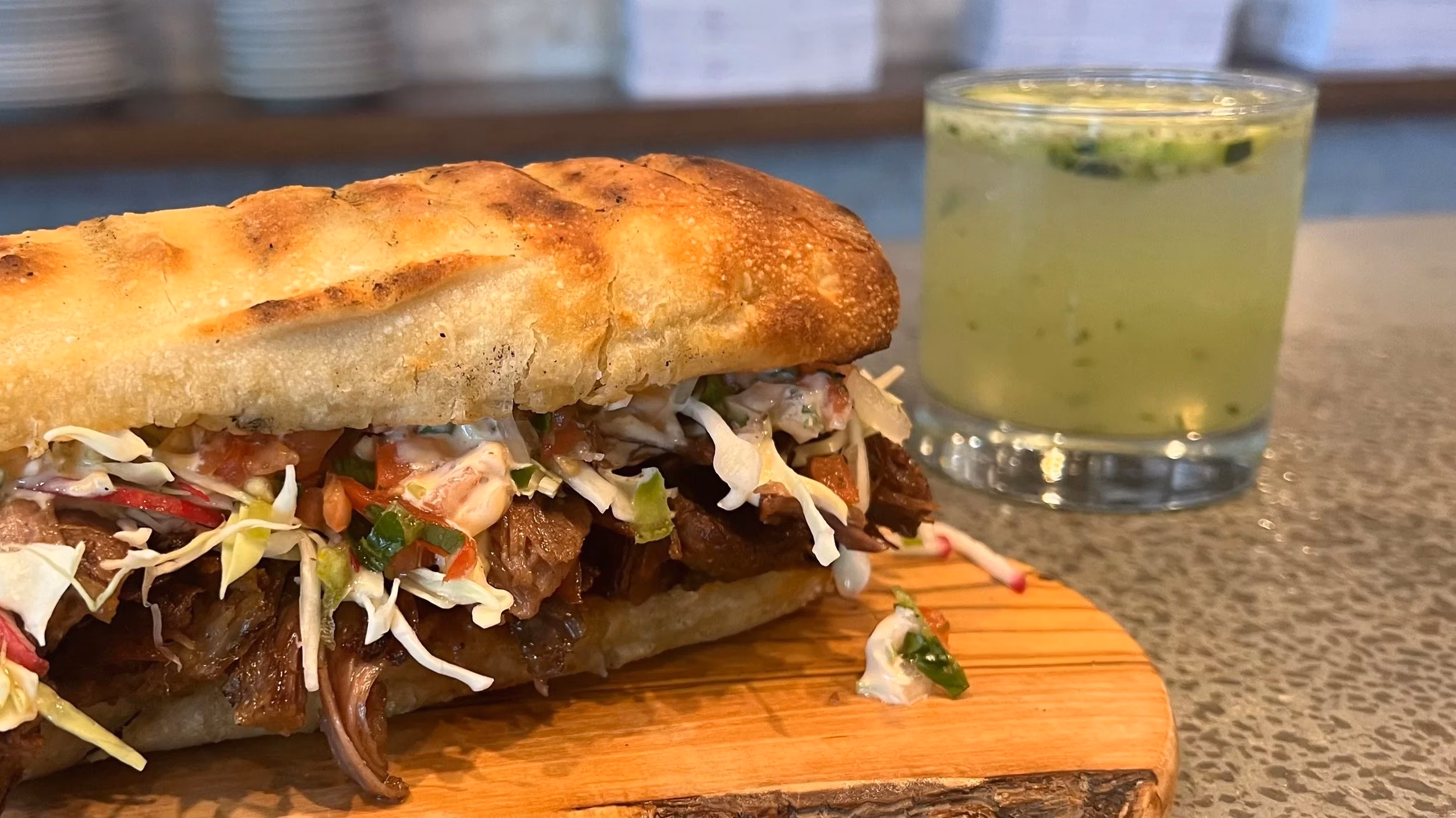 Long sandwich with meat, cabbage, and a green drink.