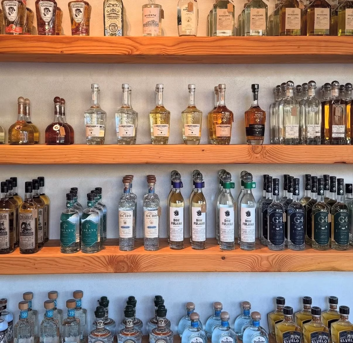 A large collection of tequila bottles on light wooden shelves.