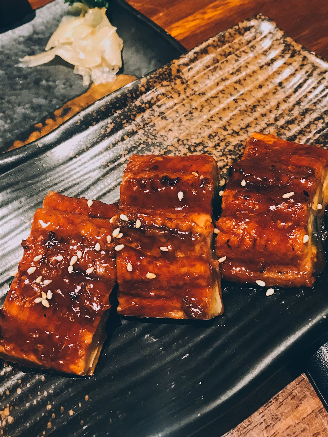 Three grilled unagi pieces with glossy sauce and sesame seeds.