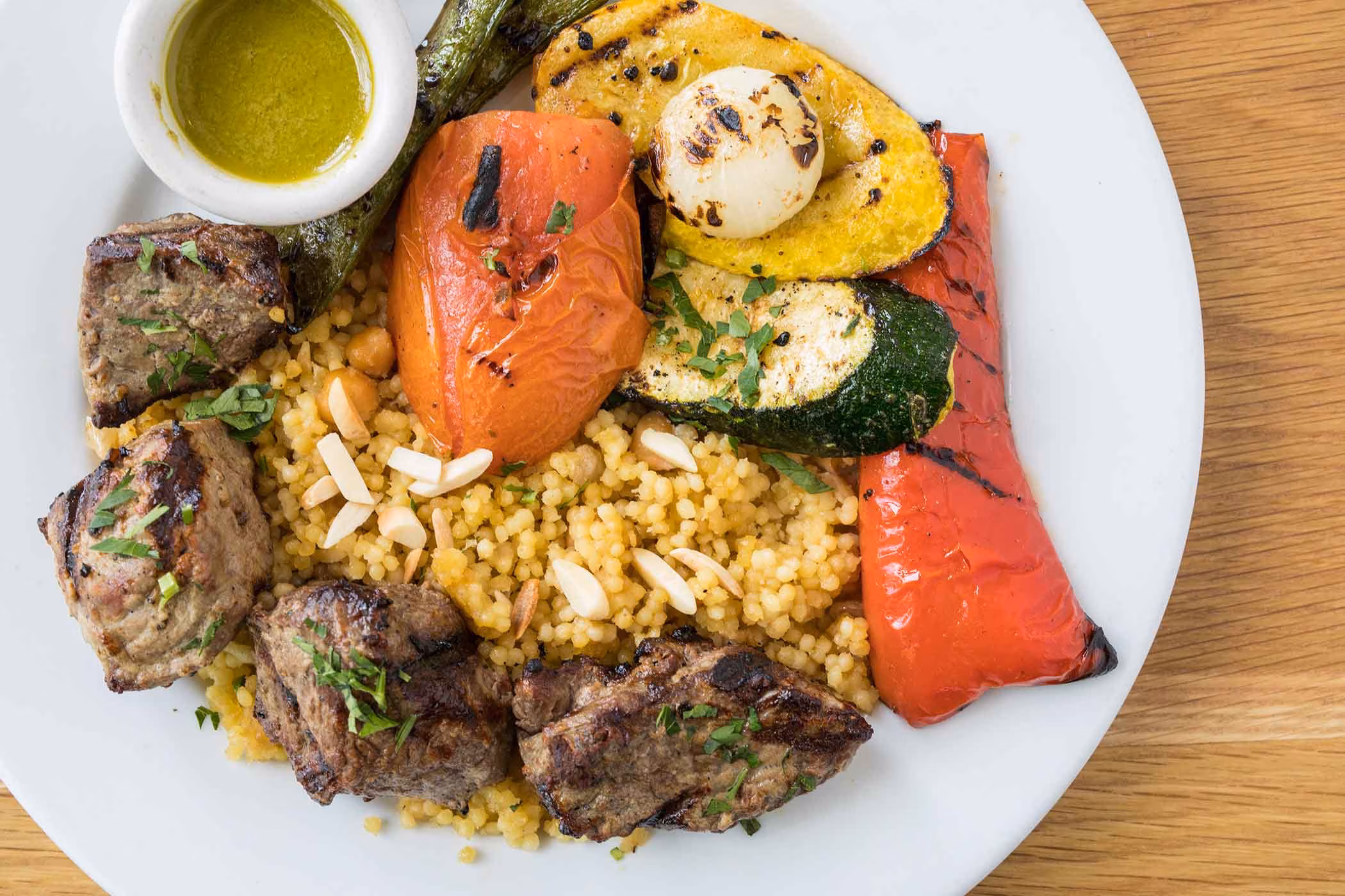 Grilled meat, couscous, grilled vegetables, and green sauce on a plate.