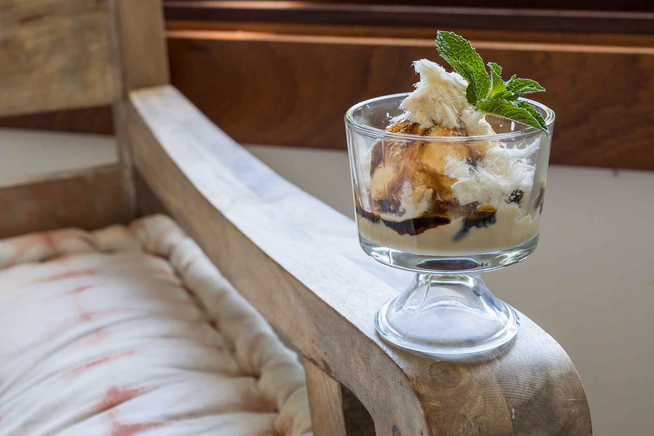 Dessert in a glass with mint on a wooden chair armrest.