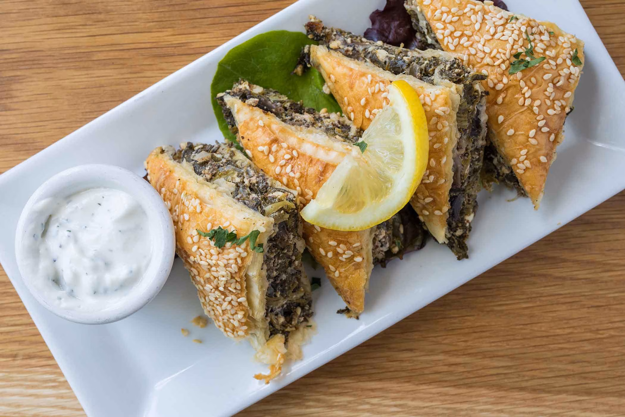 Triangular pastries with dark filling, sesame seeds, lemon, and white sauce.