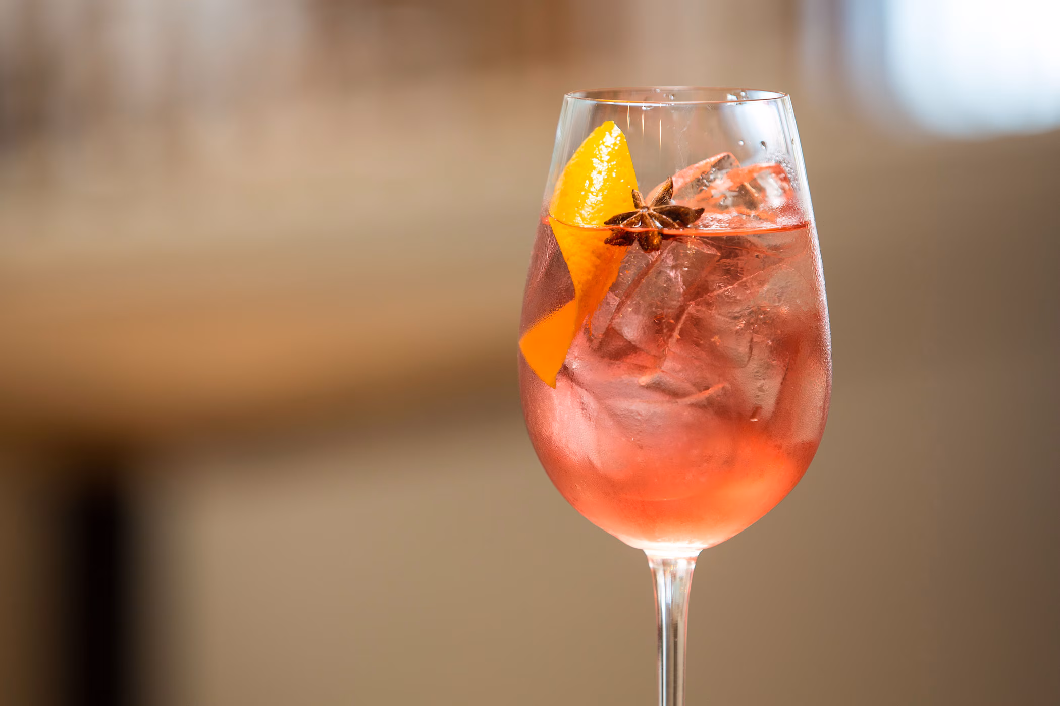 Red cocktail with ice, orange garnish, and star anise in a glass.
