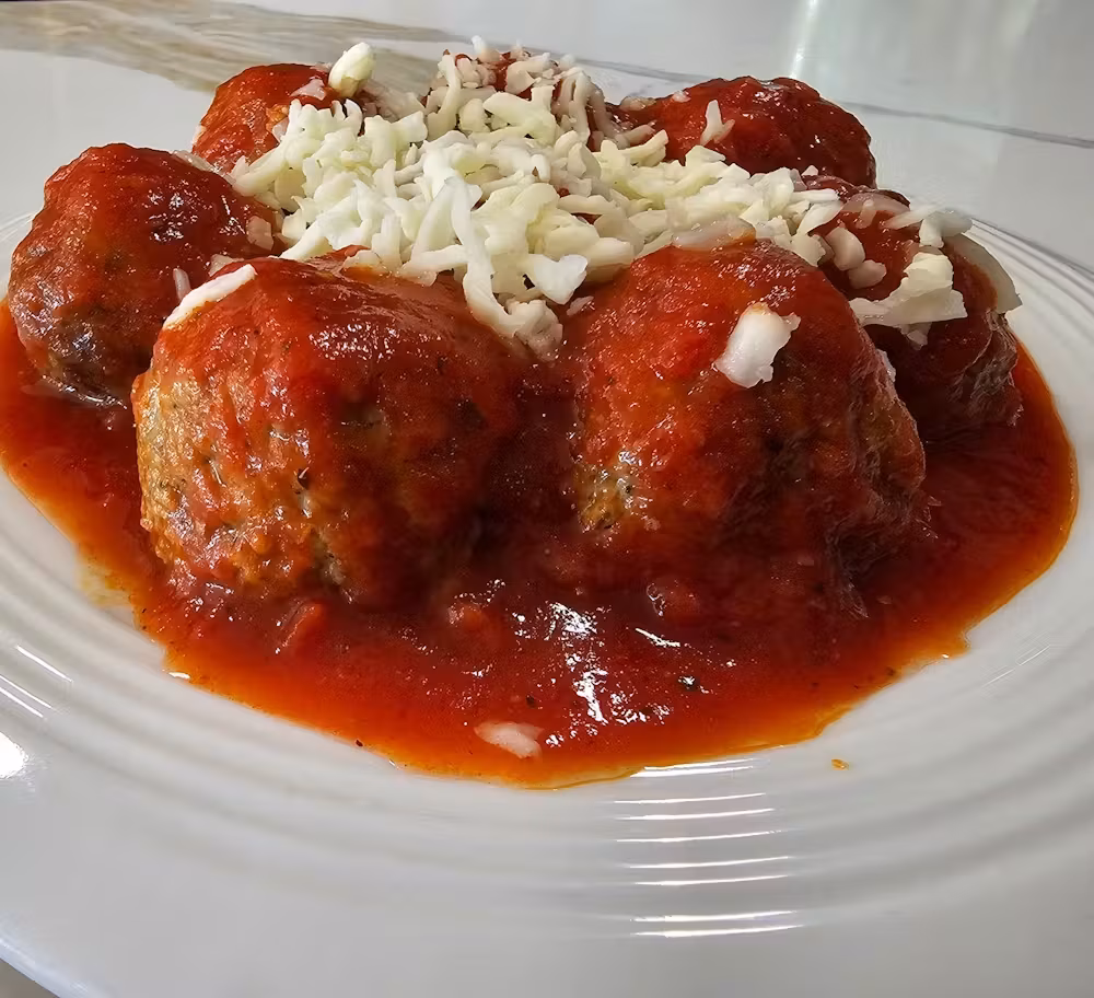 A plate of meatballs in red sauce and shredded white cheese.