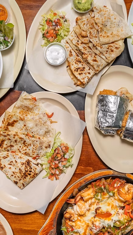 Table spread with quesadillas, burritos, and shrimp fajitas.